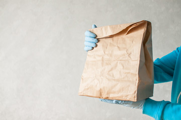 Contactless delivery of goods. The food delivery courier is holding a large paper bag in his hands. Man in rubber gloves and a medical mask.