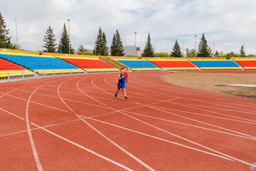 children run on the red tracks of the stadium in the summer. . empty stands of a football stadium