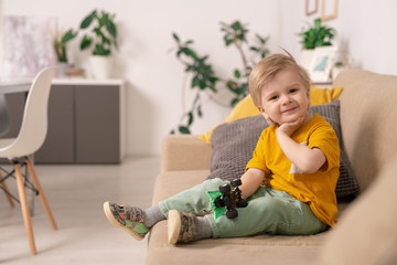 Happy cute blond boy in casualwear sitting on soft couch in living-room