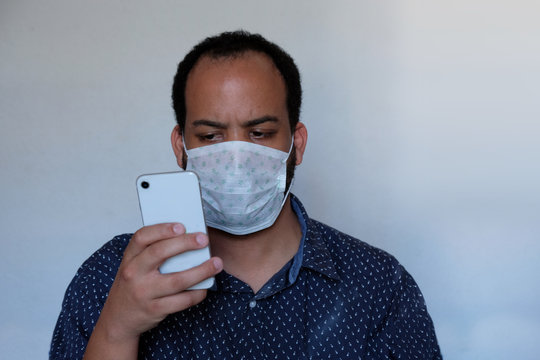 Covid-19 Corona Virus Pandemic Facemask Personal Protective Equipment Mask Mixed Race Male With Beard Wearing Blue Shirt Holding No-brand Smart Phone Reading News Worried Face