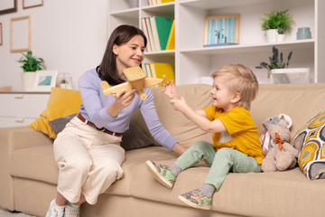 Pretty young woman in casualwear showing wooden airplane to her cute little son