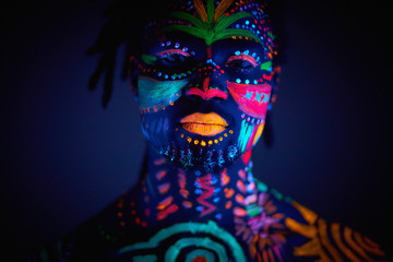 luminous portrait of young man in the UV rays on dark background, fluorescent prints on shirtless body, unusual cosmic mysterious paints