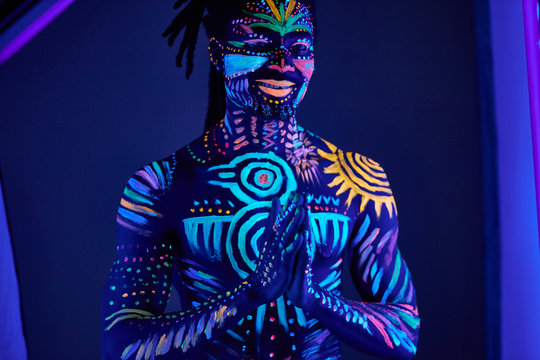 handsome young african guy with fluorescent prints on chest and other parts of body glowing in neon lights, uv rays. male fashion model posing, cosmic prints and body art concept