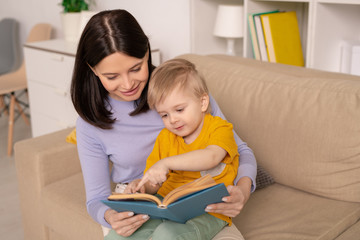 Cute little boy pointing at picture on page of book while discussing fairy tale