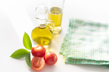 on a white background vegetable olive oil in a glass decanter. Nearby are slices of tomatoes and a green leaf.