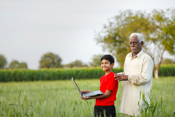 indian farmer with his grand son at wheat field, using laptop