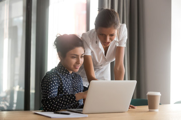 Multi-ethnic associates work together use laptop corporate application look at screen discuss task share ideas, mentor woman skilled ceo help to indian apprentice, give advice, explain program concept