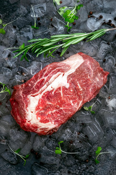 Raw fresh rib eye beef steak on ice with herbs and rosemary