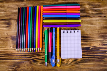 Different school stationeries (pens, notepad, pencils, felt tip pens and ruler) on a wooden background. Top view