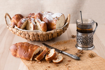 Sliced fresh bread and a vintage knife. Tea in a glass cup with a cup holder nearby. Crumbs of bread. Light wooden background. Side view. Closeup