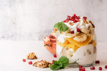 fruit salad with pomegranate, walnuts and fresh fruits in a jar on rustic concrete background front view