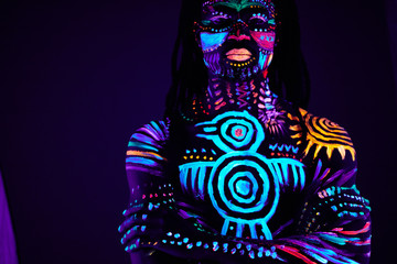 mysterious african male with fluorescent body art glowing in dark space. fashion model posing at camera, he feels the rebirth of the soul