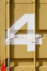 White silk-screen printing of number 4 on a mustard-colored shipping container