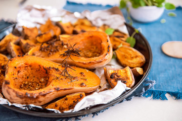Close up baked roasted grilled whole orange pumpkin butternut squash halfs and sweet potato slides with herbs on the baking sheet on blue napkin. Vegetarian and vegan food diet. Healthy eating concept