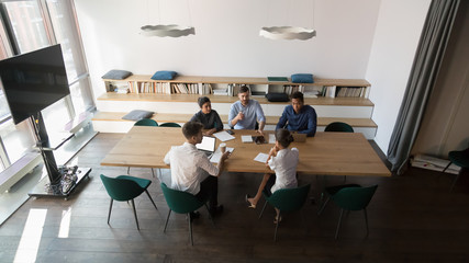 View from above in spacious modern board room gathered multi-ethnic businesspeople clients and representative planning future work collaboration conditions or coworkers discuss startup project concept