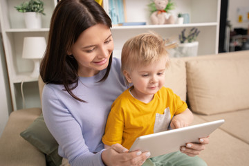 Happy young mother and cute little son looking through photos in tablet