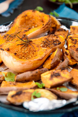 Close up baked roasted grilled whole orange pumpkin butternut squash halfs and sweet potato slides with herbs on baking sheet on blue napkin. Vegetarian and vegan food diet. Healthy eating. Vertical