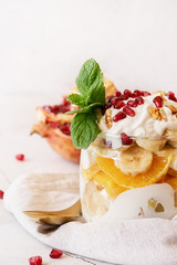fruit salad with pomegranate, walnuts and fresh fruits in a jar on rustic concrete background front view