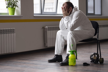 Tired of working day disinfector in a protective suit and mask. Resting after work. The fight against coronovirus.