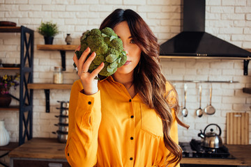 A portrait of nutritionist with a broccoli in the hand. Beautiful women in a yellow dress.