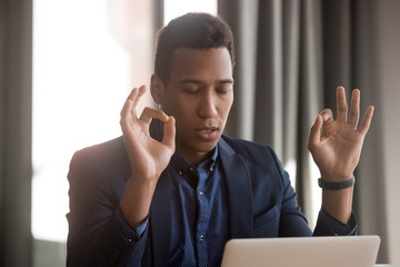 Mixed race businessman sitting at desk workplace closed eyes folded fingers mudra symbolic gesture relief stressful situations, control negative emotions, improve self-control, reduce fatigue concept