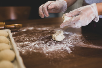 Hands of a woman making dough with plastic gloves on the table