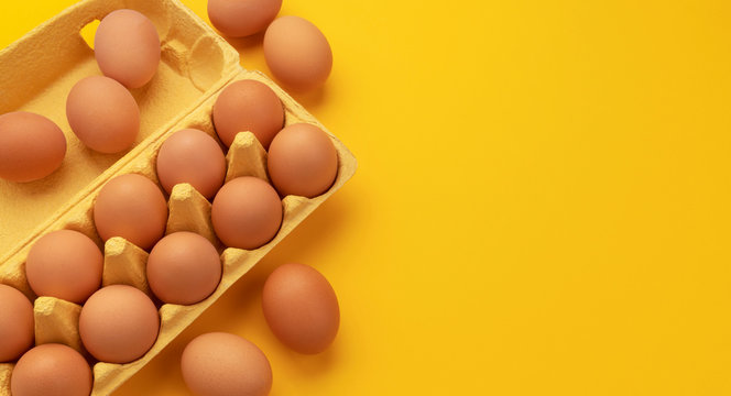 Brown chicken eggs in cardboard box on yellow background, top view