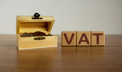 Concept word vat on cubes on a beautiful wooden table, small chest with coins.