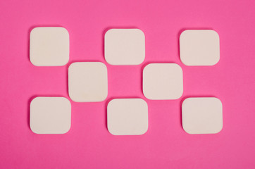 Pattern of square white cosmetic sponges on a pink background. Beauty and cosmetics concept. For magazines. Flat lay.