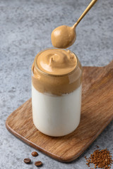Dalgona coffee in glass with spoon on grey. Korean drink latte espresso of instant coffee. Vertical shot.