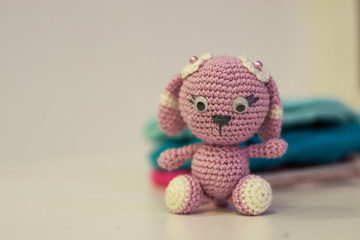Amigurumi hare of pink color, sitting on a white background. Needlework concept.