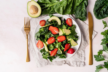 Avocado, spinach and strawberry salad top view on white background
