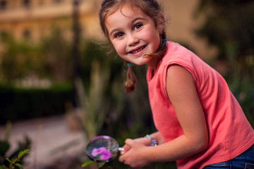 A portrait of kid girl looking at flower through magnifier. Childhood and education concept