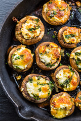 Baked champignons mushrooms, filled with cheese, parsley and roasted garlic in black bowl.