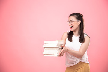 Portrait of a young woman with glasses on a pink background with books in her hands .