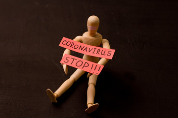 Figure of wooden man sits and asks coronavirus to stop. Pandemic, panic, recovery, red words on a...