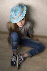 Fototapeta premium A girl in jeans and a blue hat sits on the floor.