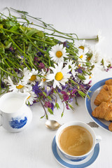 Summer morning breakfast. Cup of hot coffee, croissants and bunch of wild flowers in white background. Vertical picture