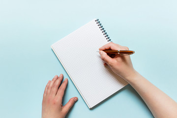 Top view mockup template with female hands writing with a Parker pen in spiral notebook laying on blue background.