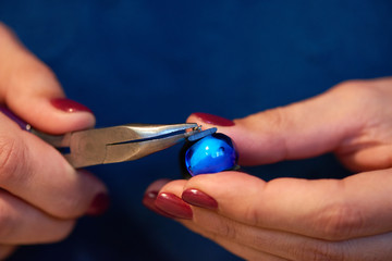 Hands of artisan with pliers fixing blue bead between two ends of leather piece