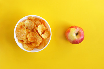 Plate with potato chips and a whole apple on a bright yellow background.