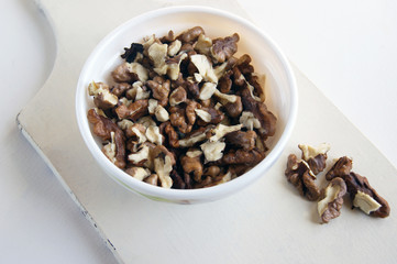 Peeled walnuts in a white cup on a wooden board on a white background.