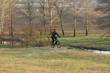 Cyclist in shorts and jersey on a modern carbon hardtail bike with an air suspension fork standing on a cliff against the background of fresh green spring forest