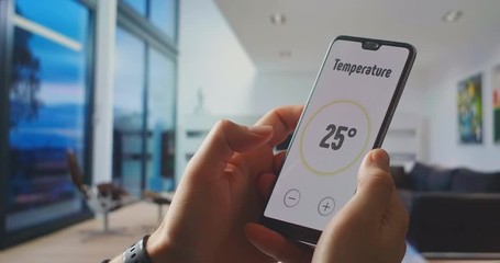 Smart home, application on the phone. A man manages various parameters of his home from a smartphone. Smart home. Man holding phone with app smart home on screen in room house - Powered by Adobe