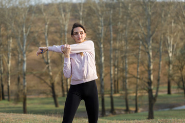 A young slim athletic girl in sportswear performs a set of exercises. Fitness and healthy lifestyle  against the background of green spring pasture hills.