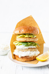 Delicious healthy crispy fish burger with greek yogurt-based sauce with lettuce and cucumber. White background, close-up, selective focus, copy-space