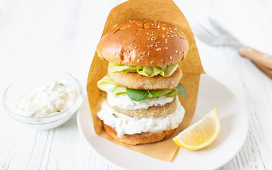 Delicious healthy crispy fish burger with greek yogurt-based sauce with lettuce and cucumber. White background, close-up, selective focus, copy-space