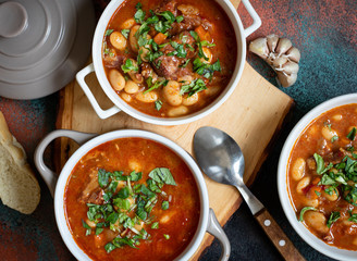 Bean soup with meat and vegetables served on a rustic board with garlic. Traditional Balkan soup or...