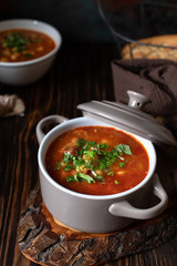 Bean soup with meat and vegetables served on a rustic board and wooden table with bread and garlic. Traditional Balkan soup Pasulj (Grah). Close-up, selective focus