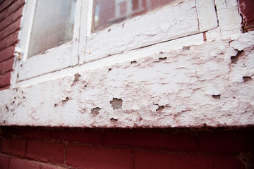 View of an old red and white building window with flaky chipped paint on the wood and bricks. Vintage window with flaky paint coming off.